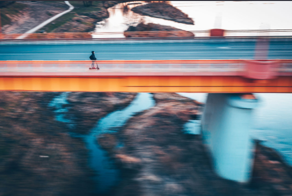 Blurred motion of person riding push scooter on bridge